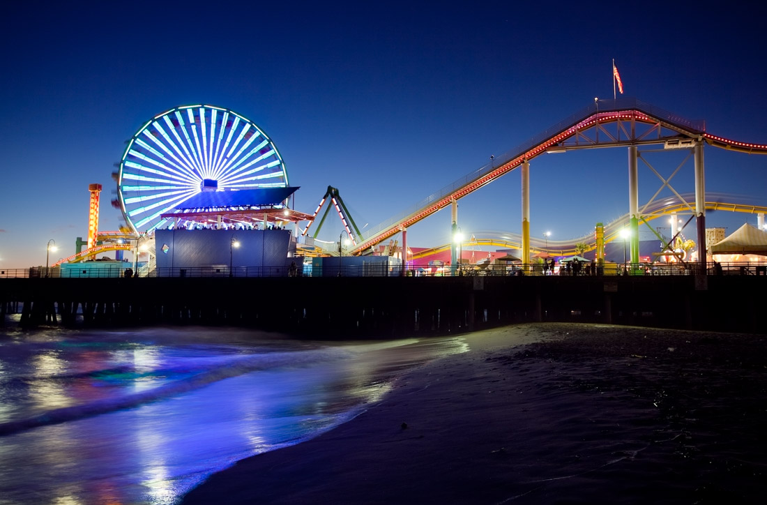Santa Monica Pier at night with ferris wheel and other rides.