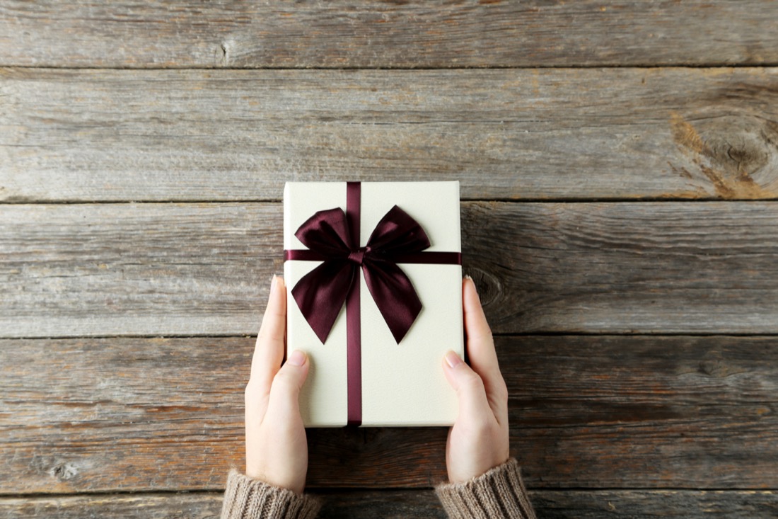 Hands holing gift in wooden background.