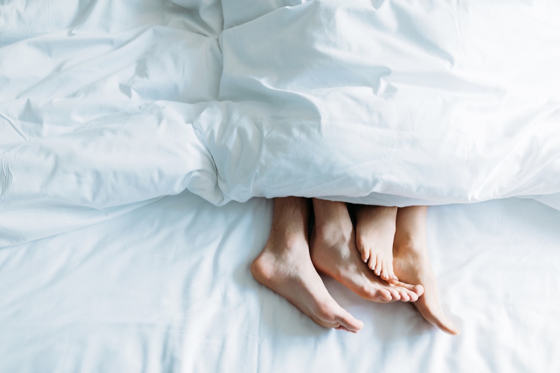 Cropped image of boyfriend and girlfriend lying in bed under blanke