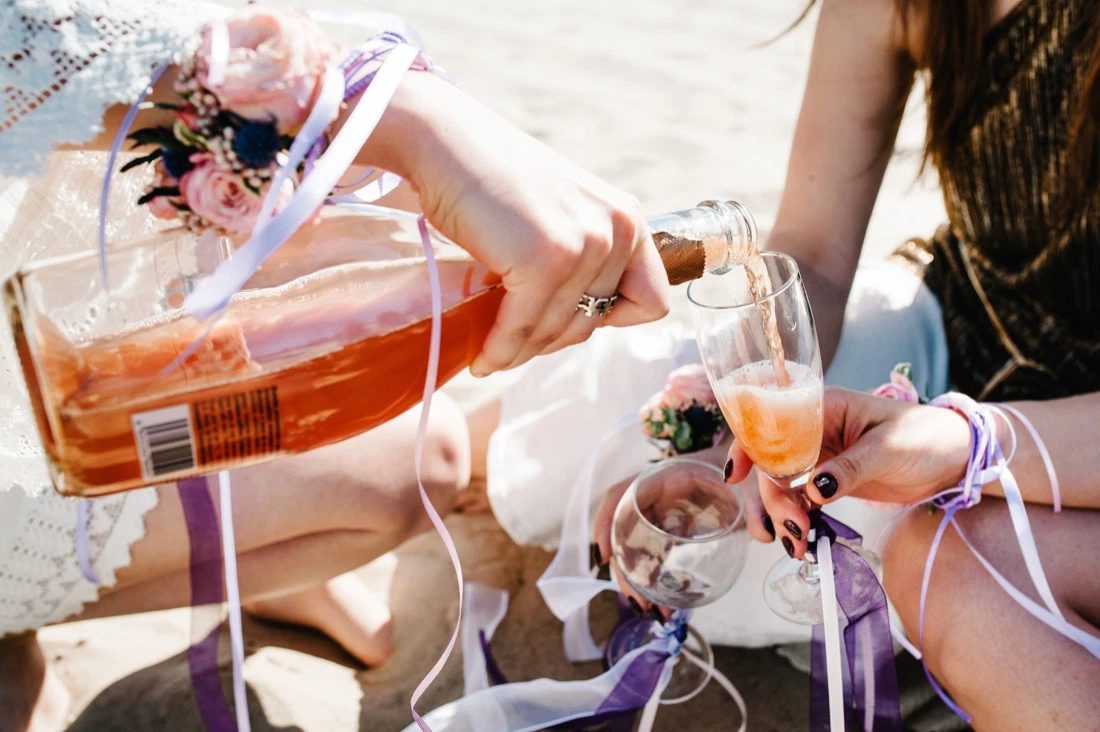 Girls pour wine on beach at bachelorette party