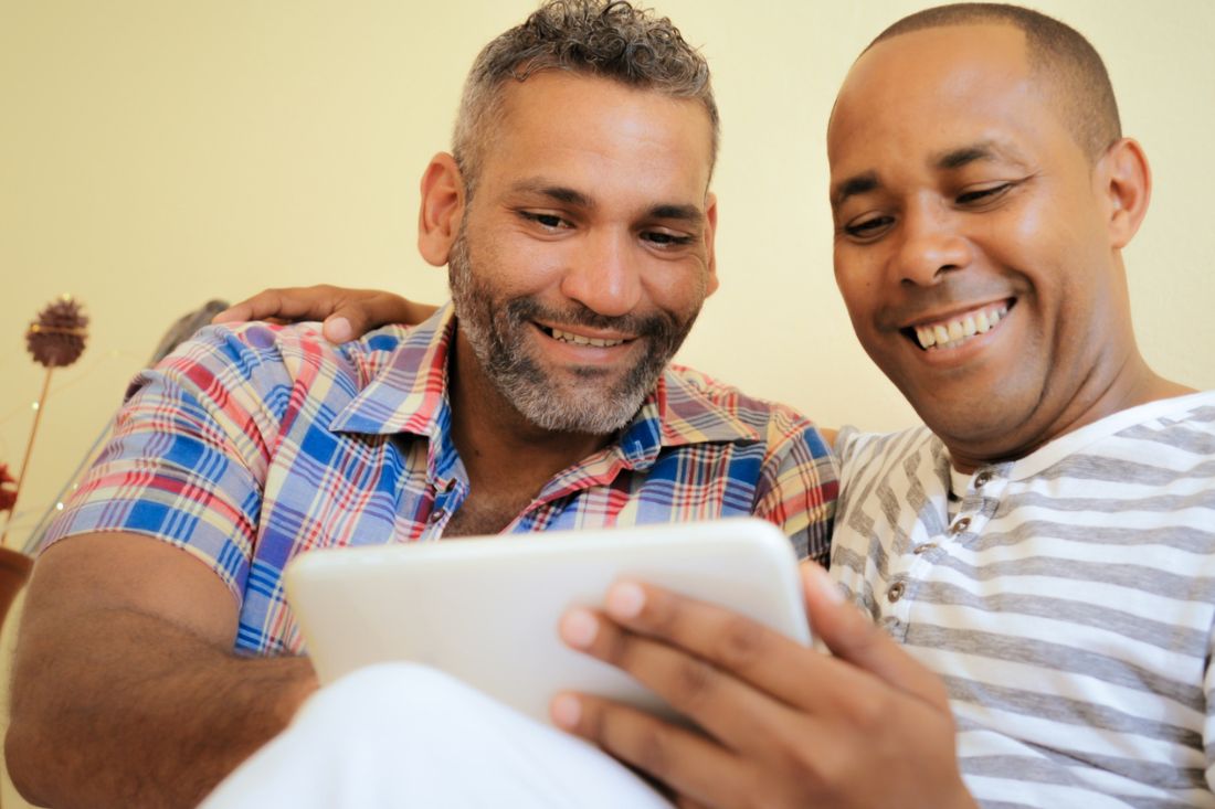 Two gay couple smiling while using a tablet