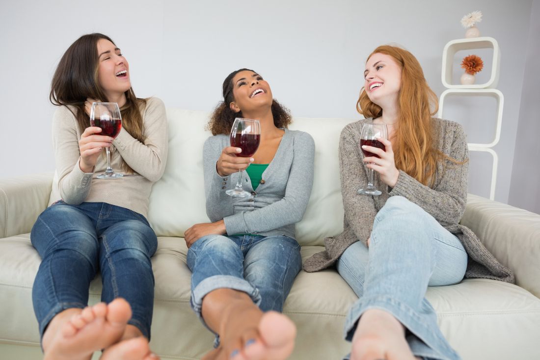 Cheerful female friends sitting on a couch and drinking wine.