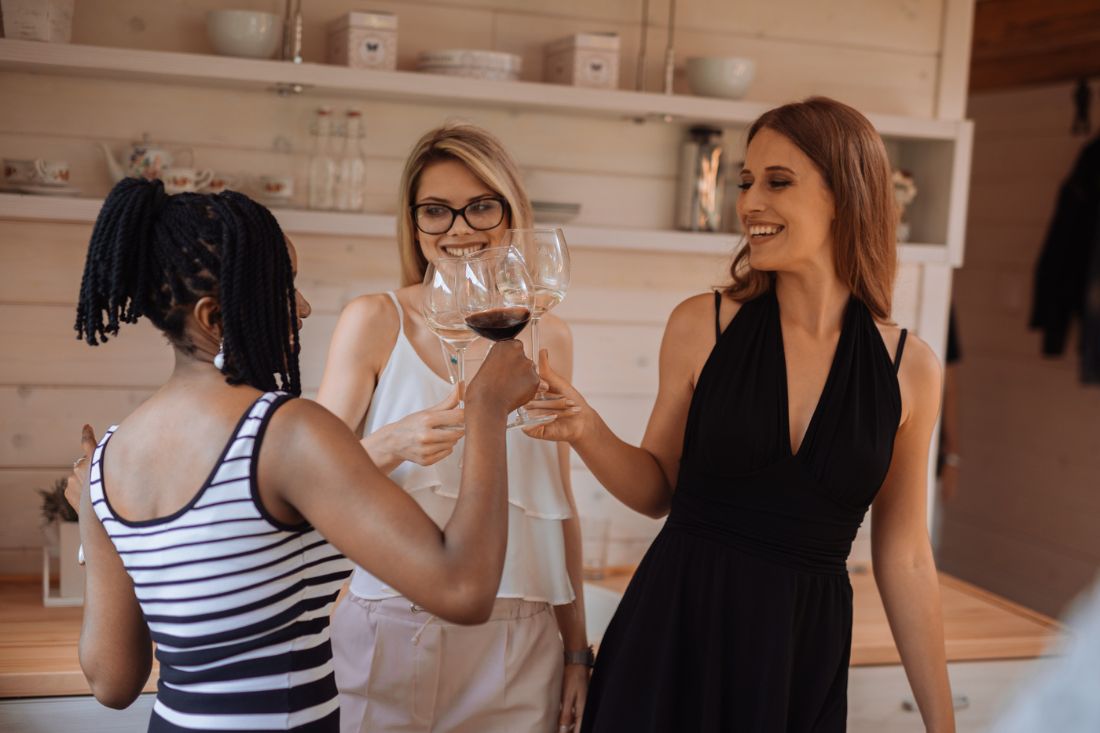 Three woman smiling and standing while having wine together.