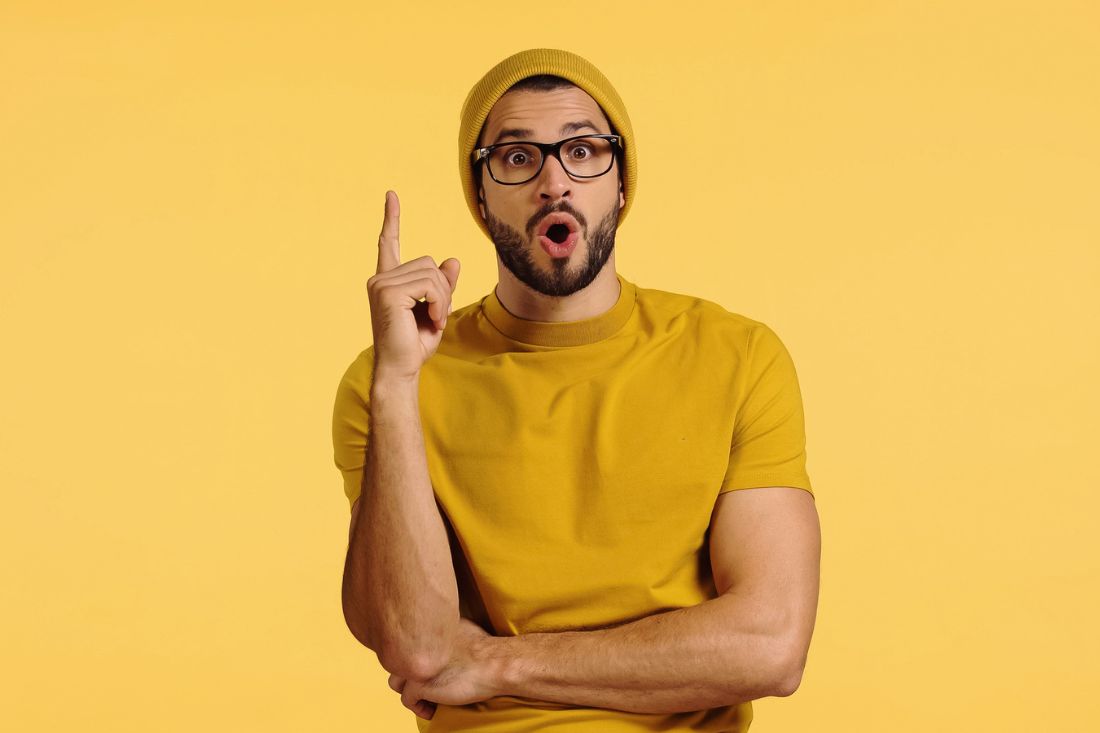Surprised man in beanie hat standing in front of yellow background.