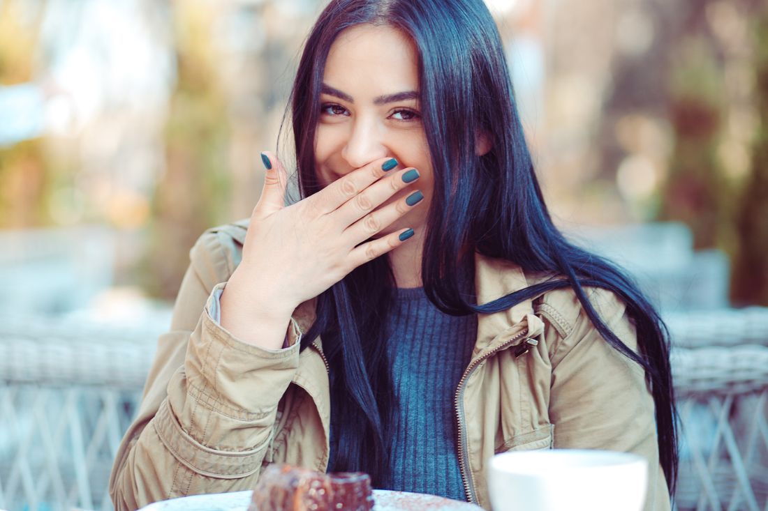 Young woman covering her mouth while smiling with food on the table.