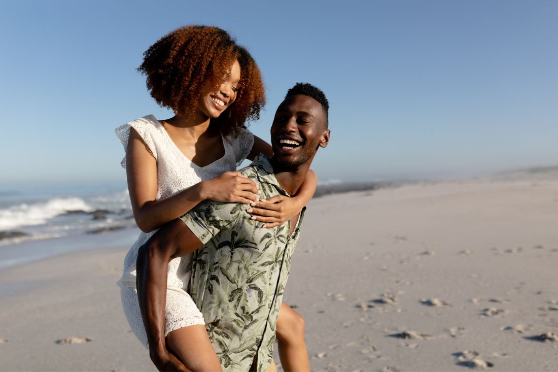 Happy mixed race couple doing piggyback ride at the beach.