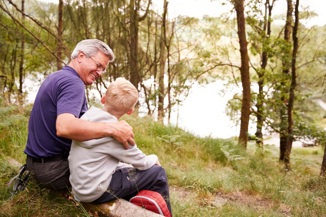 Happy grandfather and grandson sitting on a tree trunk in a forest.