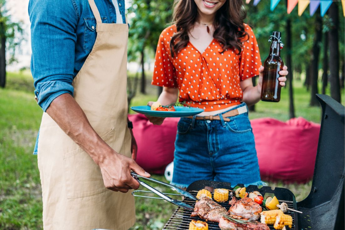 Man and woman cooking barbecue outdoors.