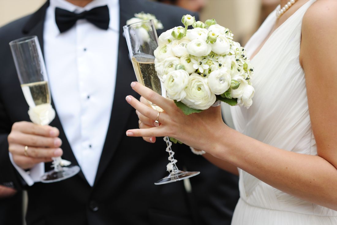 Bride with flowers and wedding ring holding champagne glass along with the groom.