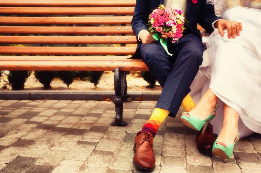 Bride and groom in bright shoes sitting on a bench.