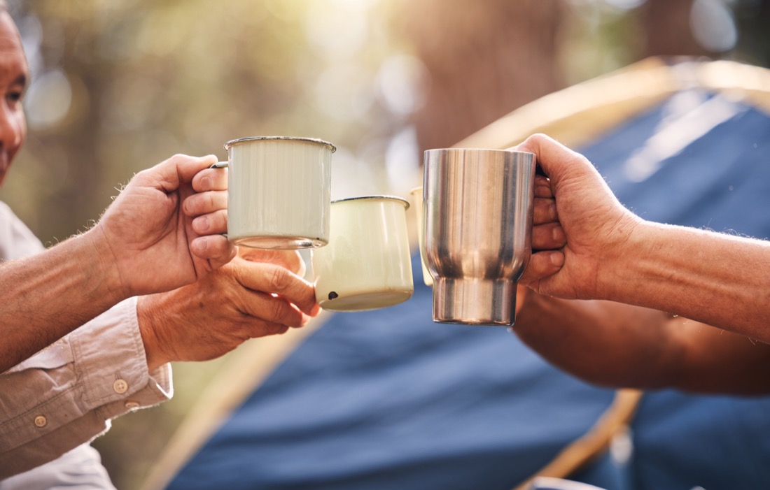 Campers toasting camping mugs with tent in background. 