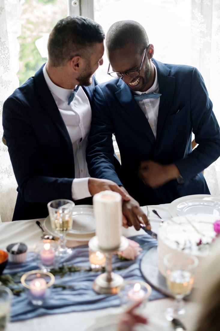 Happy gay couple cutting cake together at a wedding.
