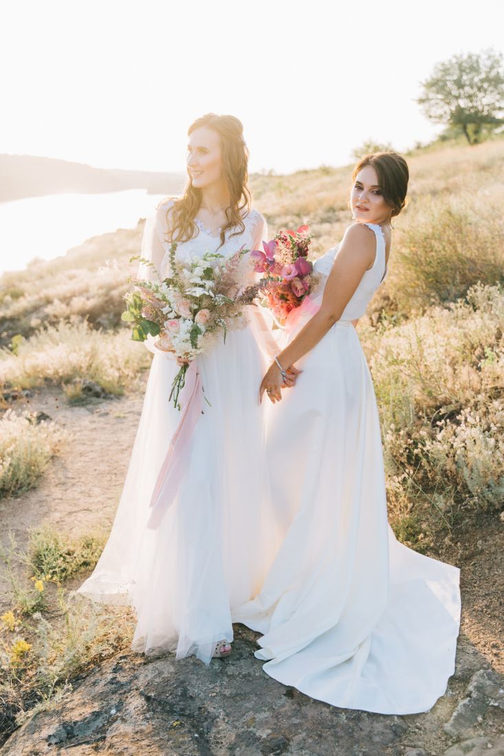 Lesbian couple in wedding dress and holding bouquet of flowers.
