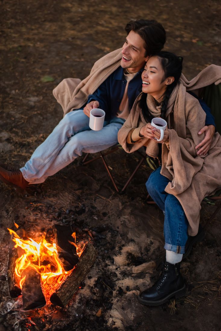 Smiling interracial couple holding a cup in front of a bonfire.