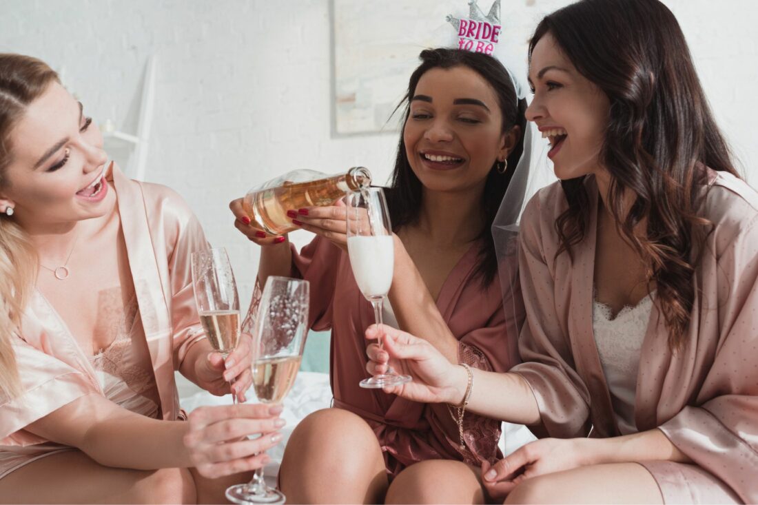 African-American bride to be pouring champagne in a glass with friends at a bachelorette party.