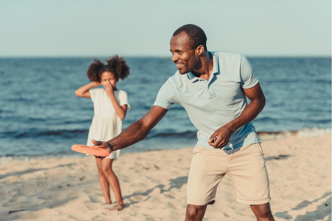 Black American father and daughter happily playing beach frisbee.
