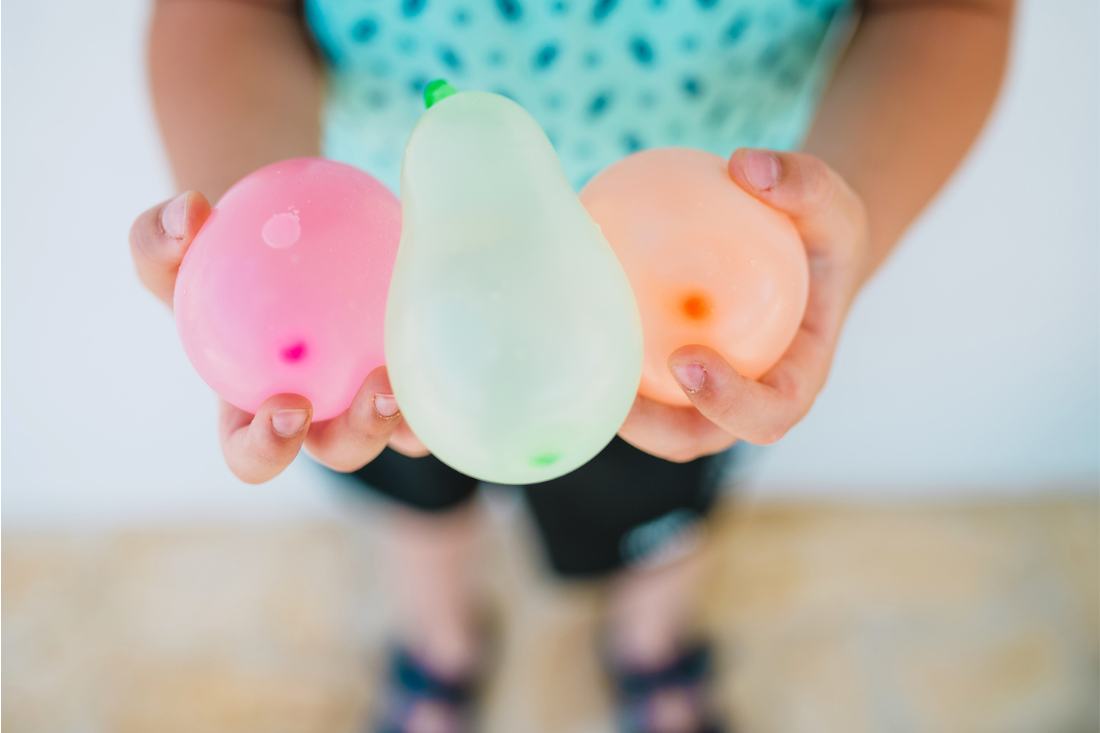 Young child holding colorful water balloons in her hand.