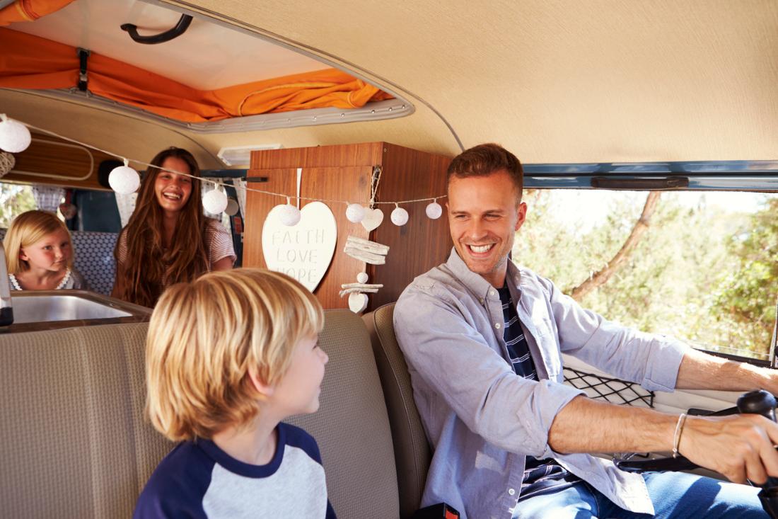 Dad happily driving a camper van with wife and two kids.