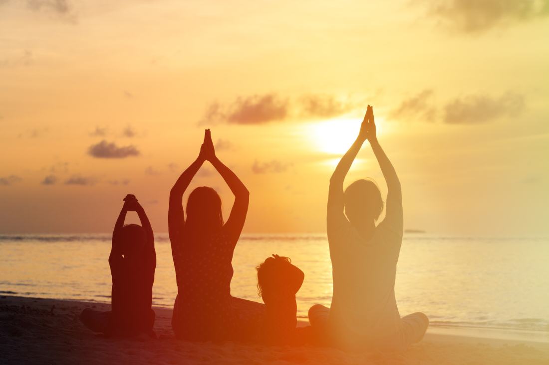 Silhouette of a family of four doing yoga at the beach during sunset.