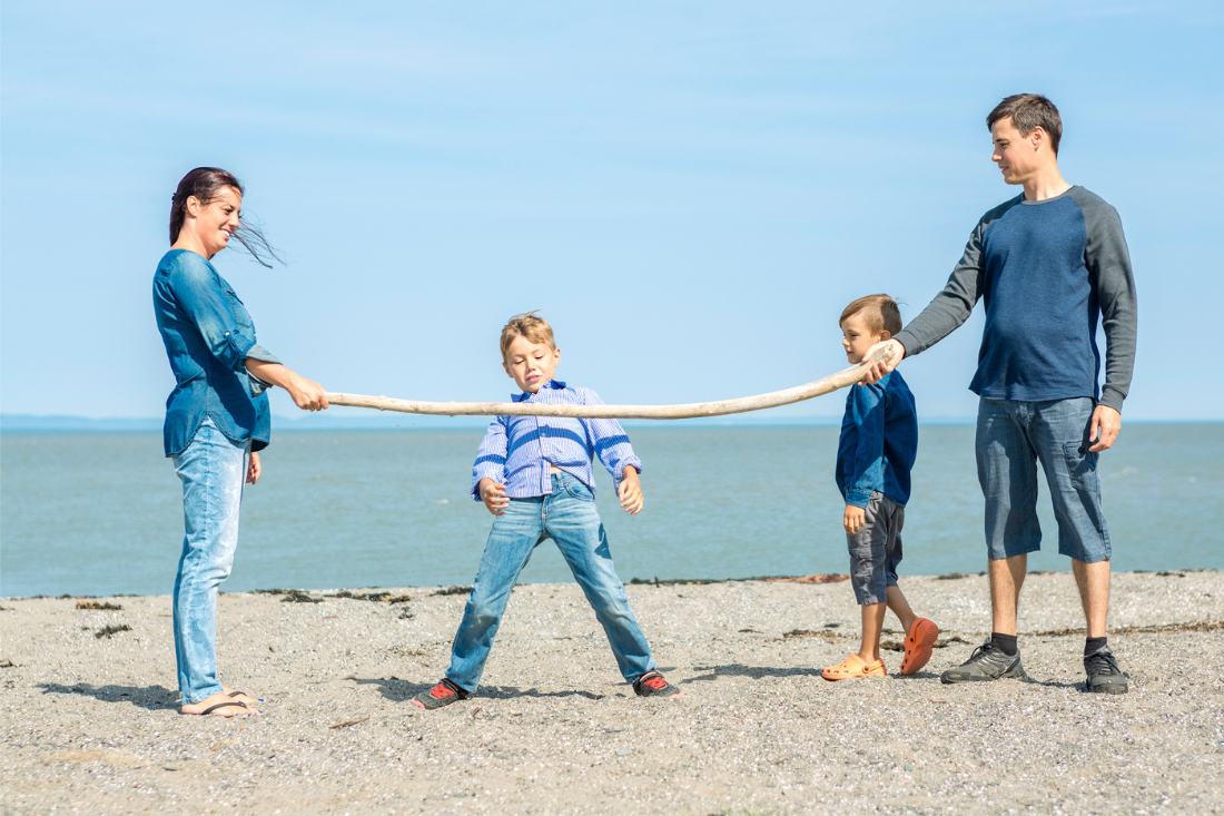 Happy family of four playing beach limbo with Mom and Dad holding the large stick.