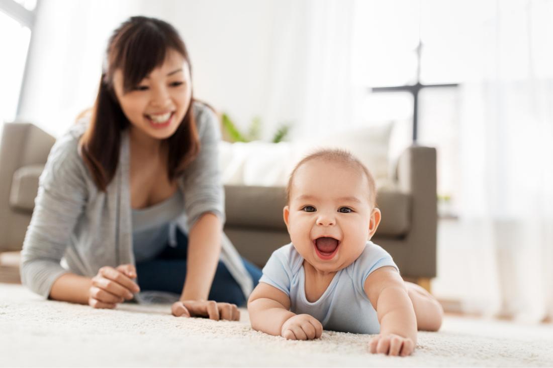 Happy Asian baby boy crawling with his mother beside him.