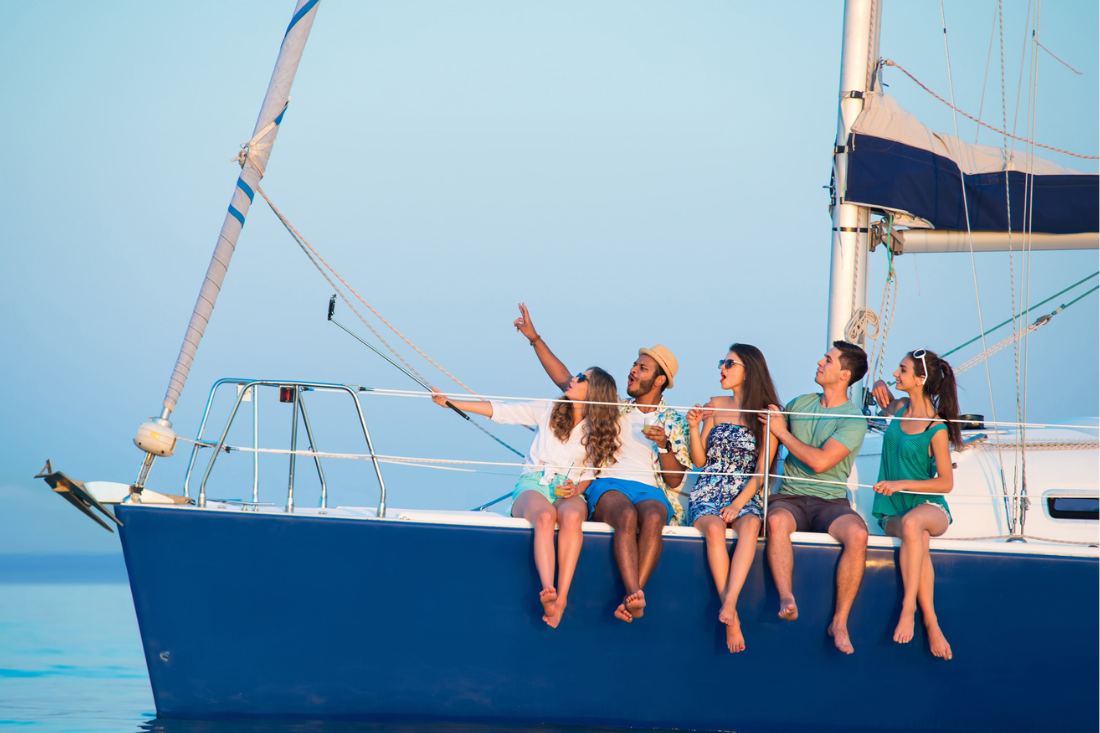 Group of five multiracial friends taking selfies on a yacht.