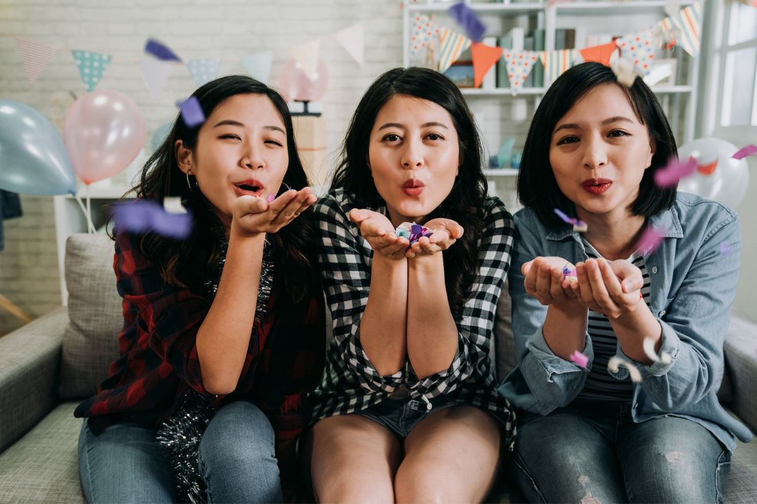Three asian girls blowing confetti.