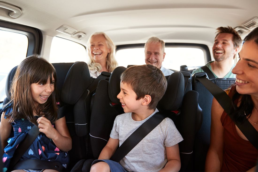 Three generation family- mom, dad, 2 kids, grandma, and grandpa happily sitting inside the car.