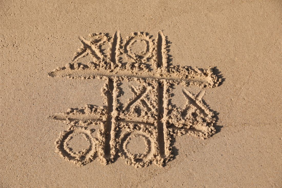 Tic tac toe game drawn on sand at the beach.