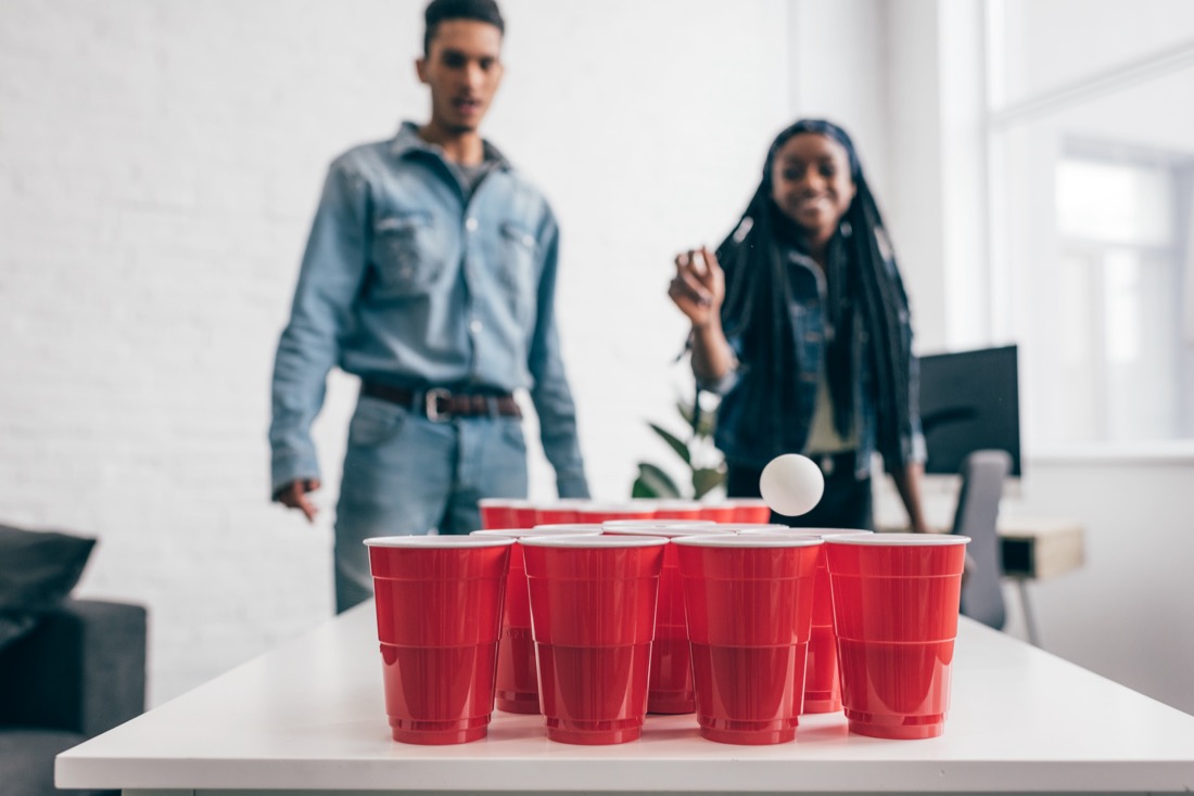 Closeup shot of ball flying in plastic cup in beer pong game and young couple standing behind