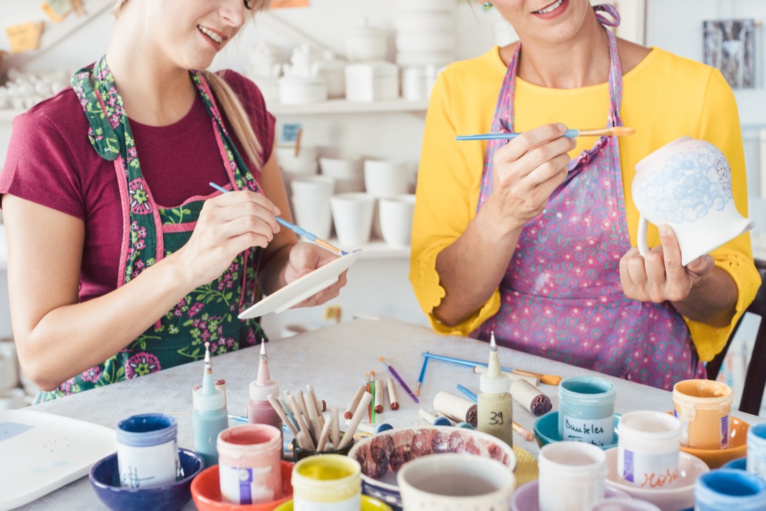 Two women painting own ceramic tableware in DIY workshop